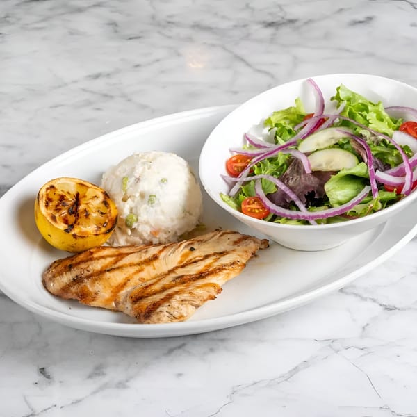 Grilled chicken, mashed potatoes, and a side salad with grilled lemon on a white plate.