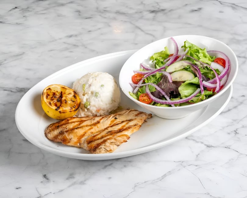 Grilled chicken, mashed potatoes, and a side salad with grilled lemon on a white plate.