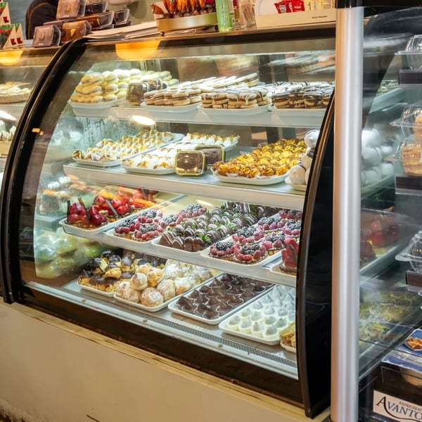 A brightly lit display case filled with various pastries, cakes, and chocolate-dipped fruits.