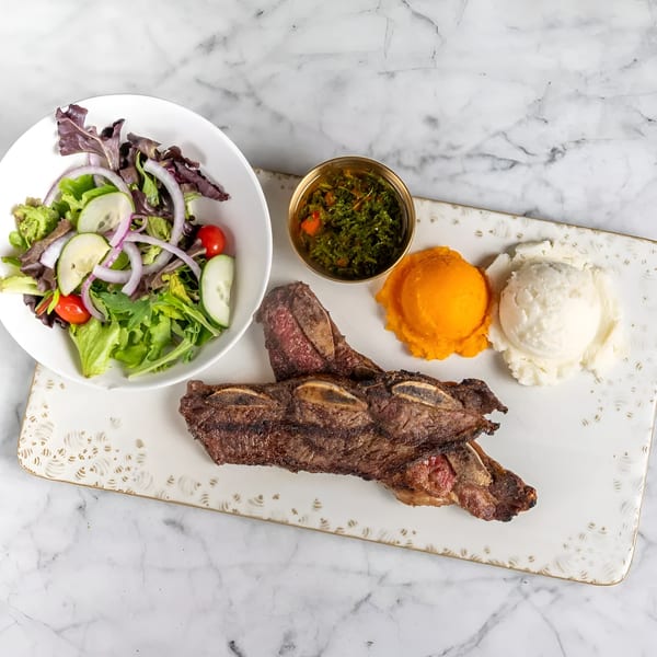 Grilled short ribs with a side salad, chimichurri, mashed sweet potatoes, and mashed potatoes.