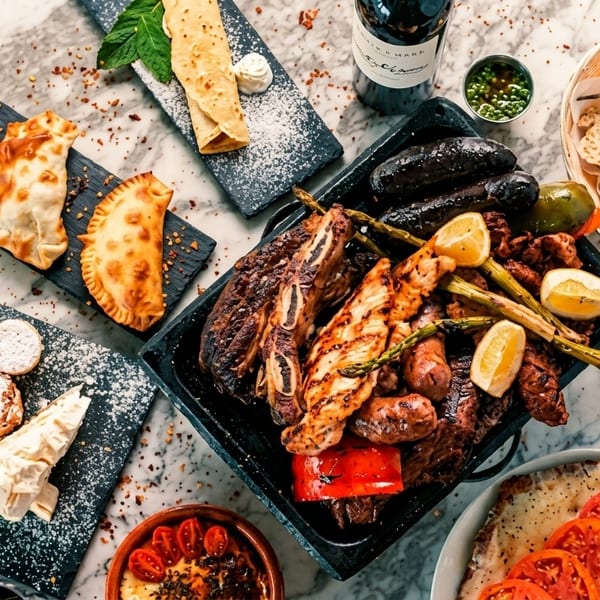 An overhead view of a marble table laden with various Argentine dishes, including grilled meats, empanadas, and desserts.